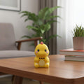 A small yellow dinosaur toy with pink accents sits on top of a fanned-out set of colorful children's educational cards on a wooden desk.